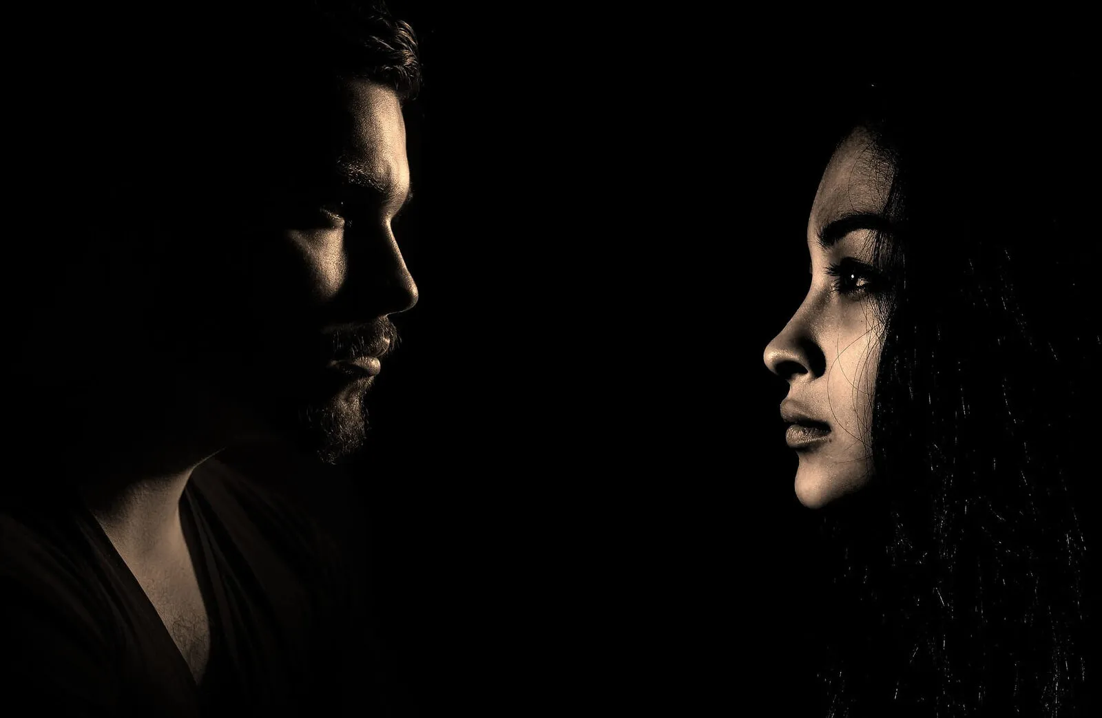 Rostros de un hombre y una mujer enfrentados en la penumbra