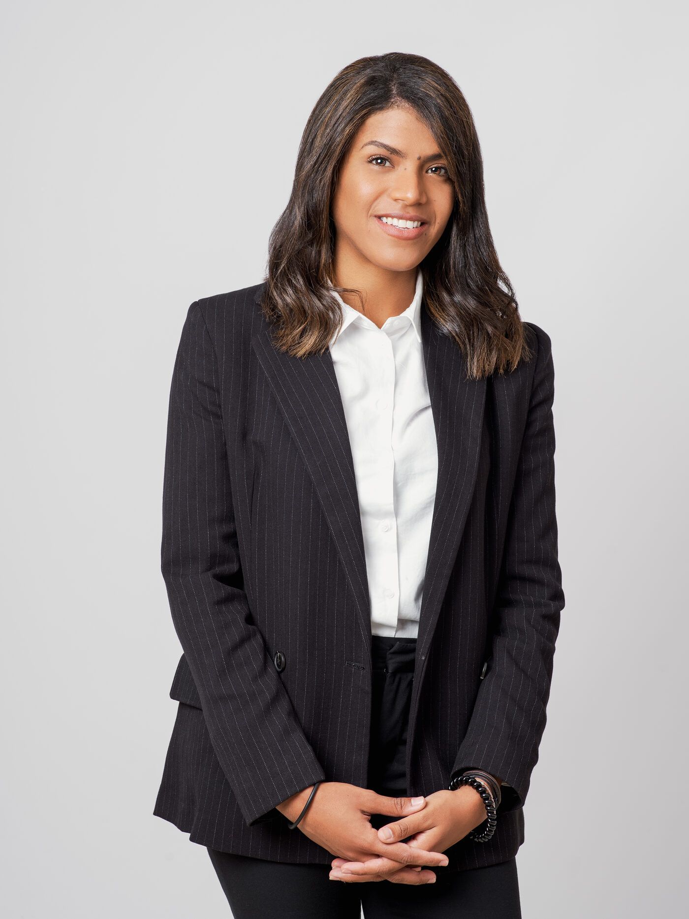 Zoraimy Sánchez de pie con americana negra y las manos entrelazadas, sonriendo